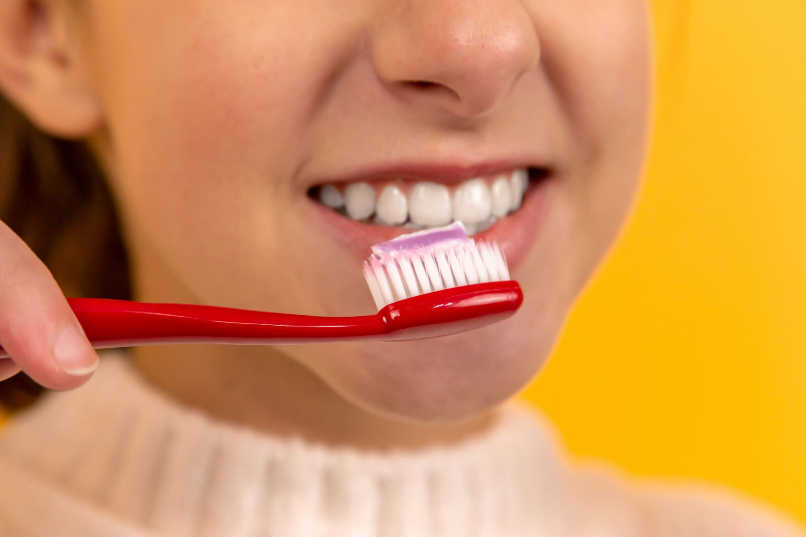 Bilde av en jente som pusser tennene med en rød tannbørste.